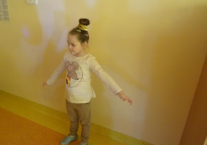 Dziewczynka stoi z rozłożonymi rękami pod ścianą.